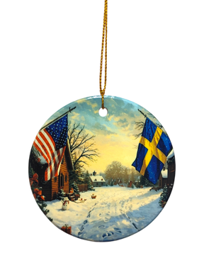 The Ornament: Wooden Village Ceramic Ornament with USA & Sweden Flags features a snowy village scene and hangs from a gold string—ideal for Scandinavian Christmas décor.