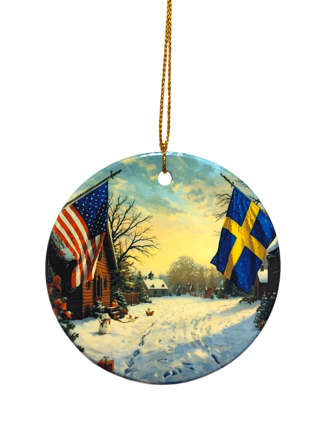 The Ornament: Wooden Village Ceramic Ornament with USA & Sweden Flags features a snowy village scene and hangs from a gold string—ideal for Scandinavian Christmas décor.