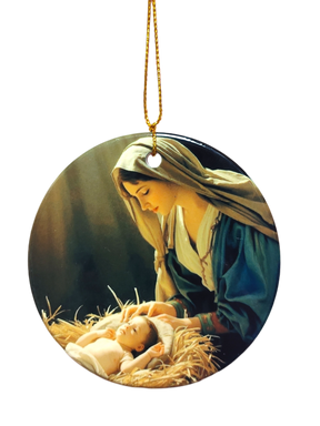 The Ornament: Nativity Scene Ceramic Ornament features a painting of a woman in a headscarf gazing at an infant on straw, with a gold hanging string—an elegant faith-inspired Christmas décor piece.