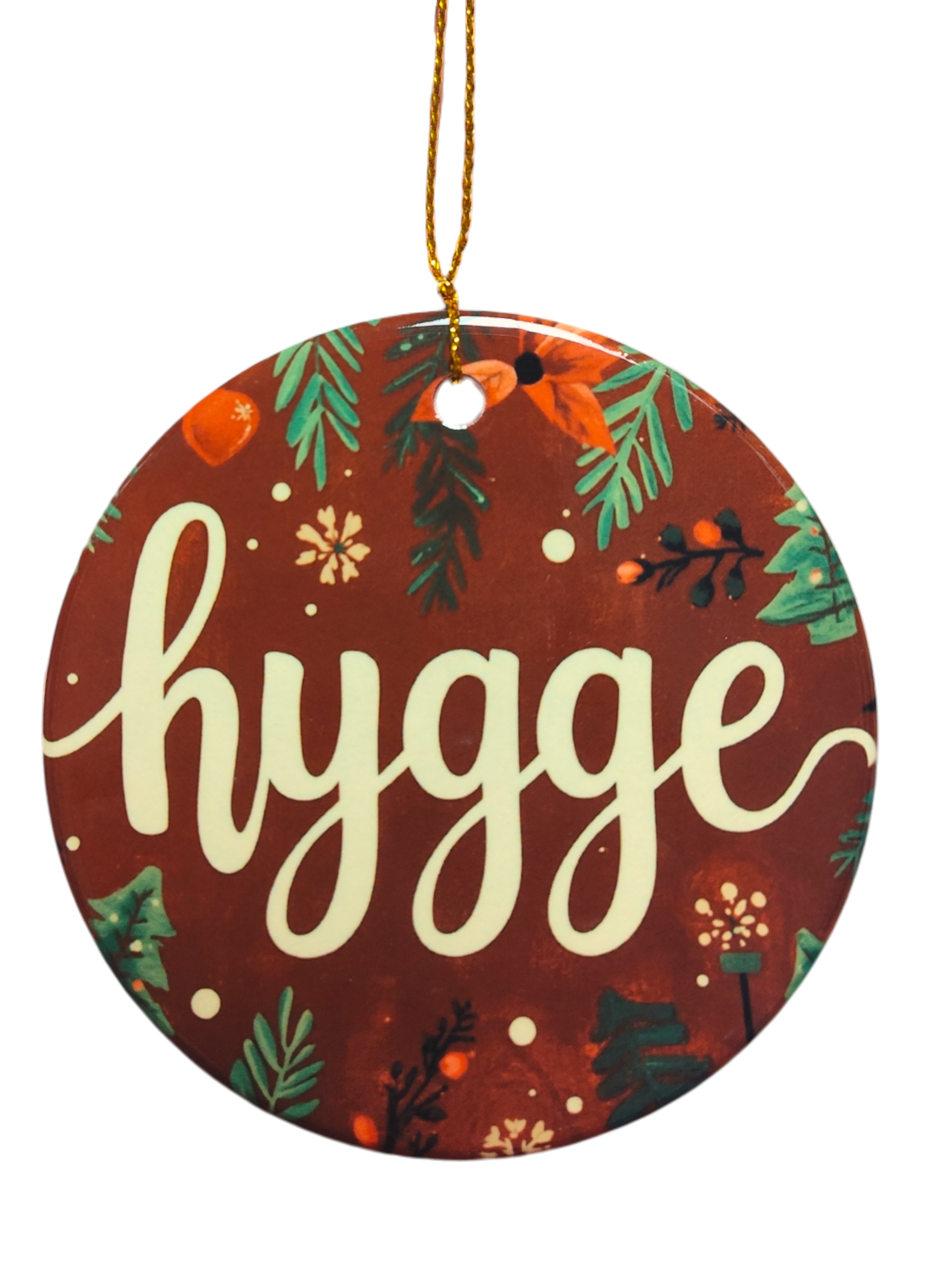 A round ceramic ornament called "Brown Hygge Ceramic Ornament," featuring a brown background and white script, hangs by a gold string—a cozy accent perfect for Scandinavian decor.