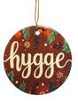 A round ceramic ornament called "Brown Hygge Ceramic Ornament," featuring a brown background and white script, hangs by a gold string—a cozy accent perfect for Scandinavian decor.