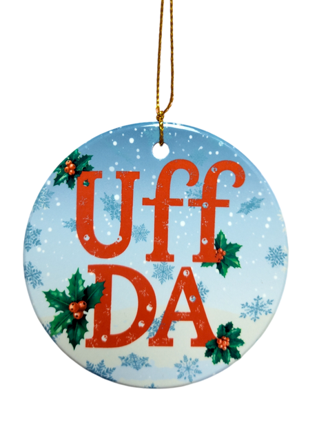 The Ornament: Uff Da Ceramic Ornament features "UFF DA" in red, holly leaves and berries, blue snowflake background, and a gold hanging string—a charming Scandinavian holiday décor piece.