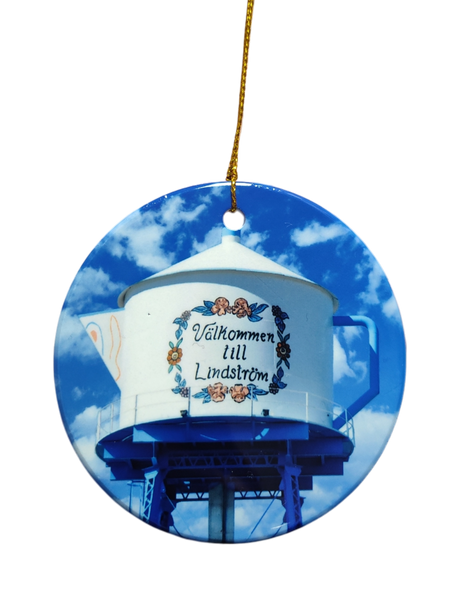 The Ornament: Valkommen till Lindstrom Ceramic Ornament features a water tower painted as a teapot with “Välkommen till Lindström” in Swedish, celebrating the city's Scandinavian heritage against a blue sky.