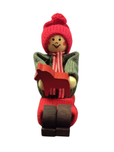 The Figurine: Handcrafted Swedish Santa Boy Sitting with Red Dala Horse features a smiling, rosy-cheeked Santa in festive attire—ideal for adding authentic Swedish charm to your Christmas decor.