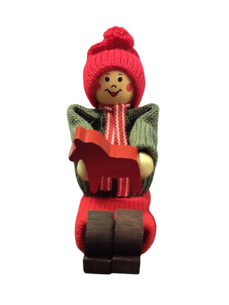 The Figurine: Handcrafted Swedish Santa Boy Sitting with Red Dala Horse features a smiling, rosy-cheeked Santa in festive attire—ideal for adding authentic Swedish charm to your Christmas decor.