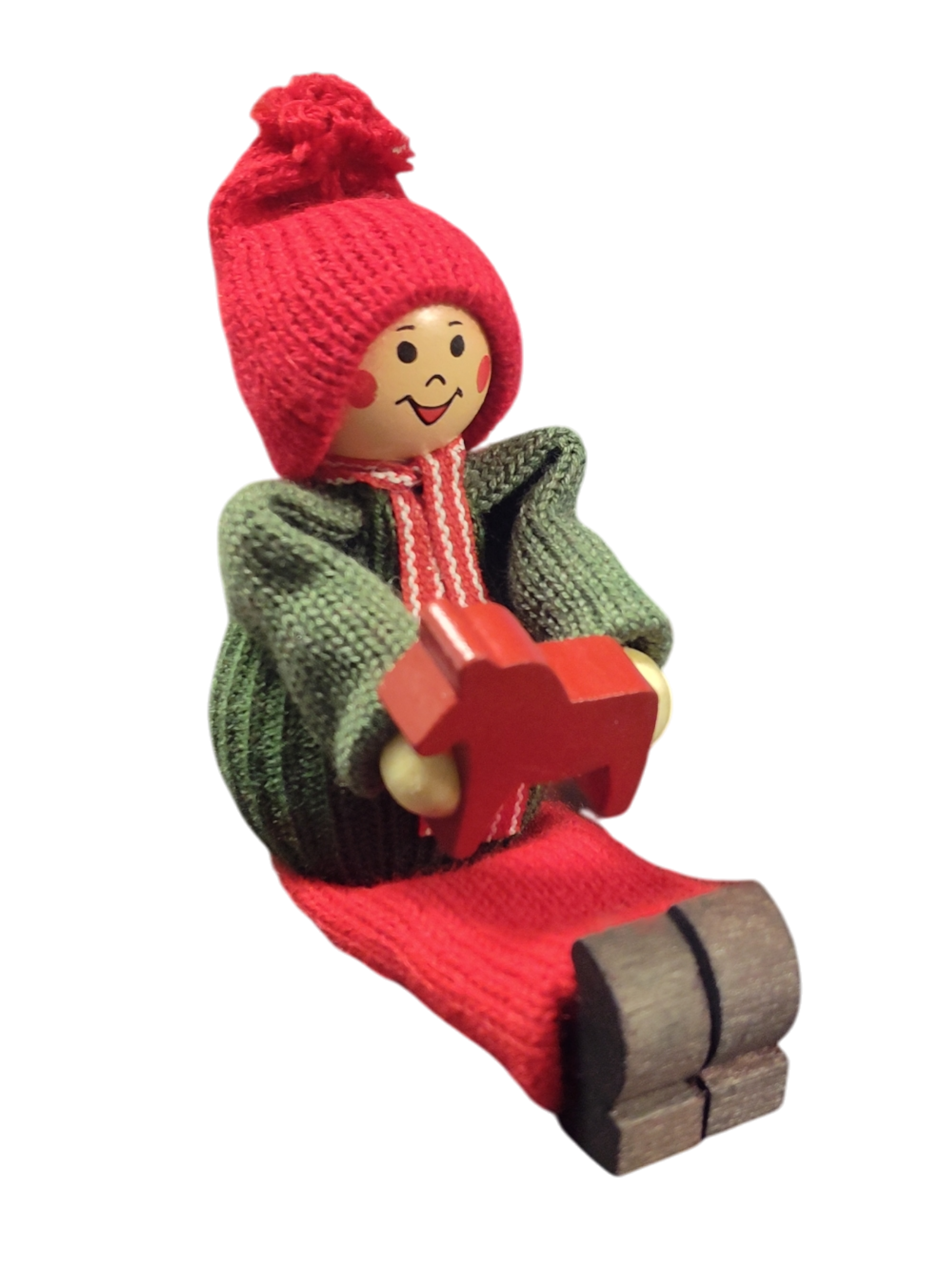Handcrafted Swedish Santa Boy figurine sits with legs extended, wearing a red hat and green sweater, and holding a small red Dala Horse—perfect for festive Swedish Christmas decor.