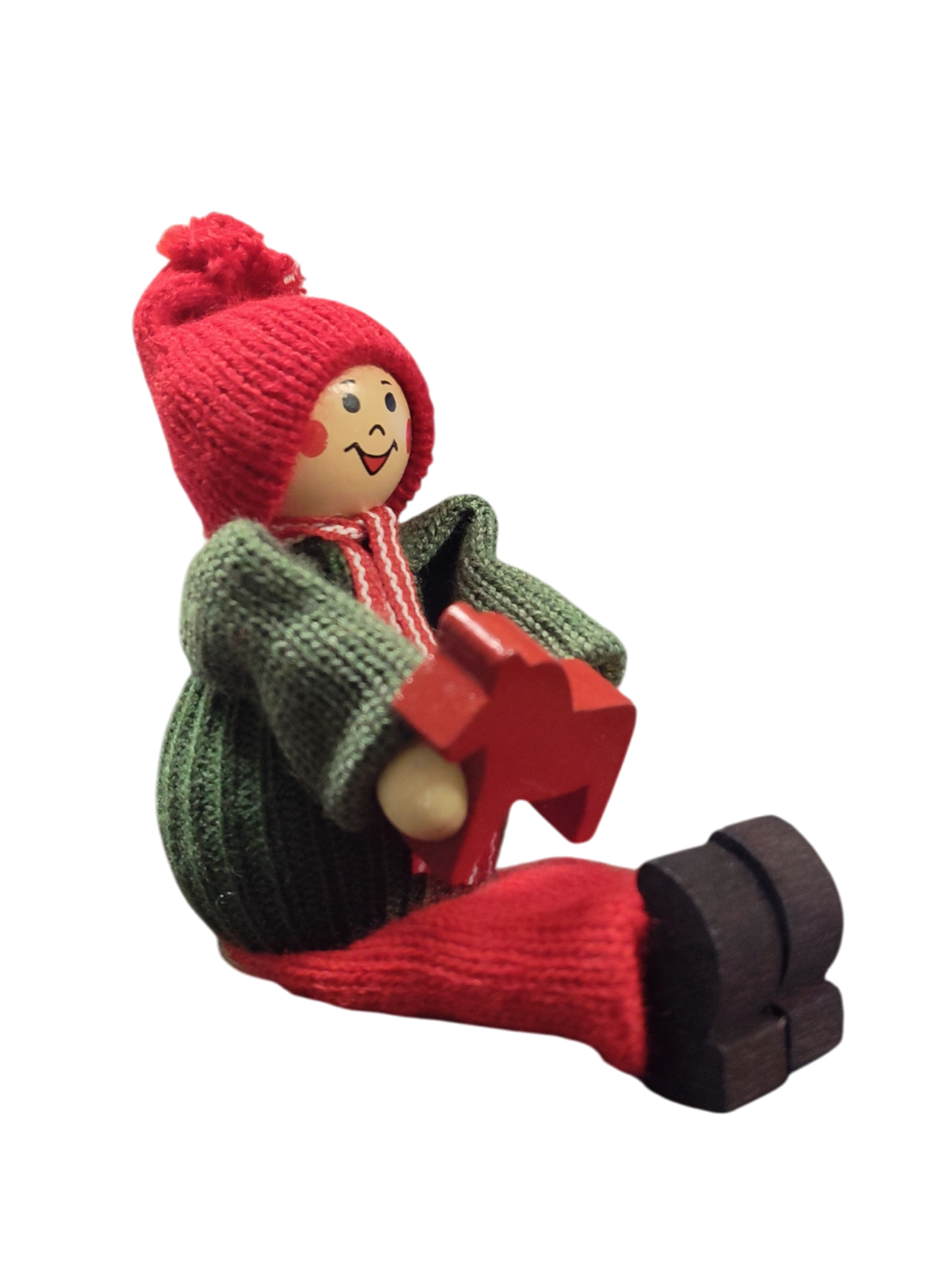 The Handcrafted Swedish Santa Boy Figurine sits holding a red Dala Horse, dressed in a green sweater, red hat, and red pants—perfect for adding Swedish Christmas charm against any neutral white background.