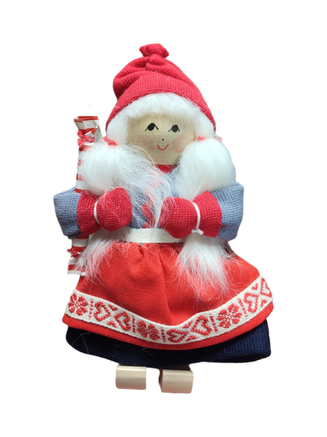The Figurine: Santa Girl in Traditional Holiday Dress Carrying a Candy-Cane Striped Package features a handcrafted Swedish design—white hair, red mittens and hat, blue and red dress—a charming addition to your Scandinavian Christmas décor.