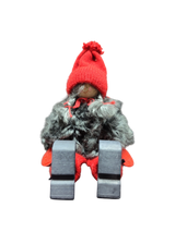 The Sitting Santa Girl Figurine features a red knit hat, mittens, gray faux fur coat, red pants, and black boots. Displayed upright against a white background, it makes a charming addition to your Christmas décor.