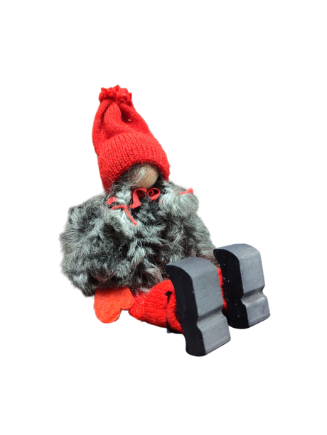 The Sitting Santa Girl Figurine features a red knit hat, red mittens, gray fuzzy coat, and black wooden shoes—handmade in Sweden and perfect as charming Christmas décor.