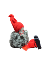 The Sitting Santa Girl Figurine features a plush gnome design with a gray beard, red knit hat, mittens, socks, and black shoes. Handmade in Sweden, it’s a charming Christmas décor piece. Shown side view on white background.