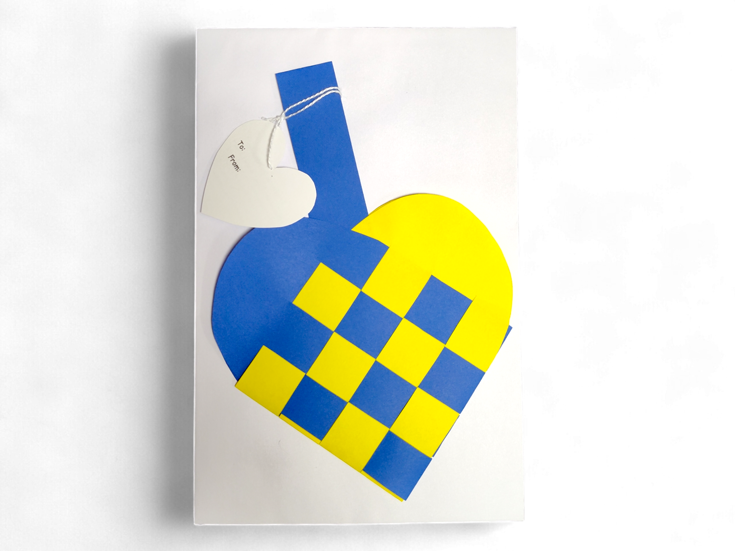 A Card: Swedish Flag Traditional Scandinavian Handwoven Paper Basket Heart with a heart-shaped tag attached by string, shown on a white background.