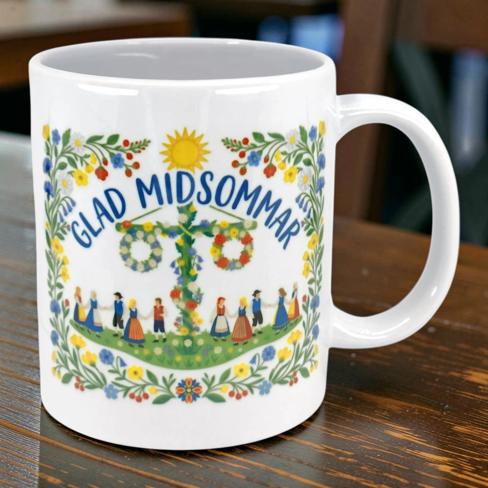 White mug with “GLAD MIDSOMMAR” text, a floral border, and illustrations of people dancing around a maypole in Swedish folk art style.