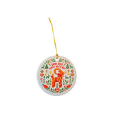 A round white ceramic Christmas ornament featuring a colorful Swedish folk art design with a red reindeer, green pine trees, red hearts, and the text 'GOD JULI GOTT NYTT A!'. The ornament hangs from a yellow string against a plain white background.