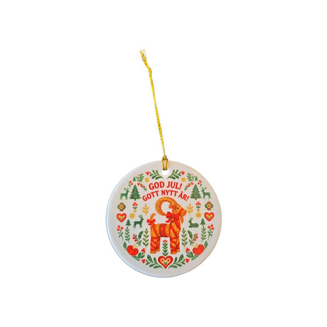 A round white ceramic Christmas ornament featuring a colorful Swedish folk art design with a red reindeer, green pine trees, red hearts, and the text 'GOD JULI GOTT NYTT A!'. The ornament hangs from a yellow string against a plain white background.