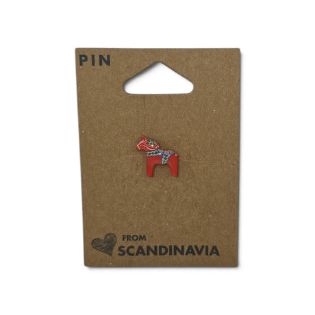 Red Dala horse lapel pin with decorative pattern, attached to brown card labeled “PIN” and “FROM SCANDINAVIA” with a small heart illustration.