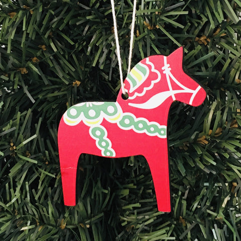 A Wooden Dala Horse ornament, painted in red with green and white patterns, decorates the Christmas tree, highlighting traditional craftsmanship.