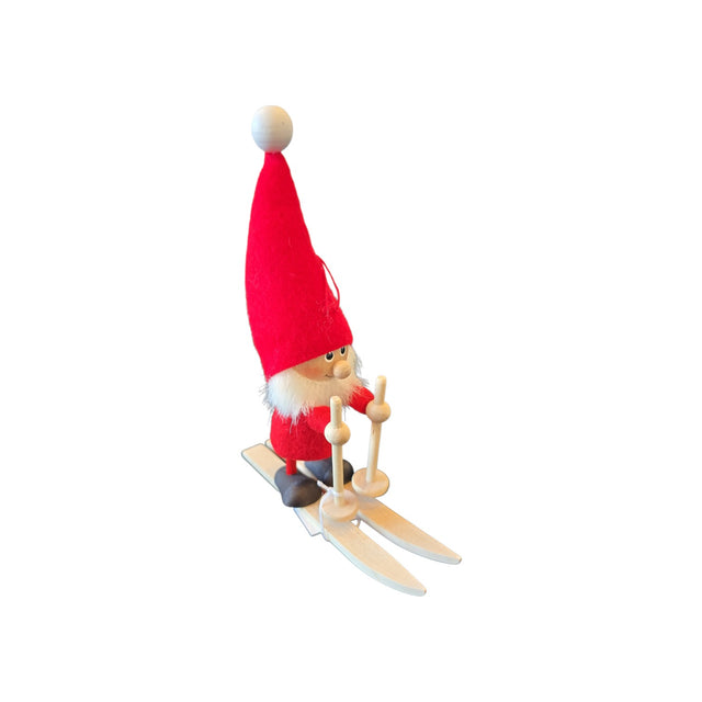 Scandinavian wooden tomte figurine with a white beard and tall red hat, standing on miniature skis and holding poles.