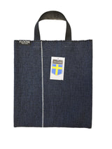 The Horredsmattan Floow Vinyl Bag (32x40cm) is a dark blue tote with black handles, a vertical white stripe, FLOOW. label, Swedish flag tag, and features the iconic Swedish vinyl rug design.