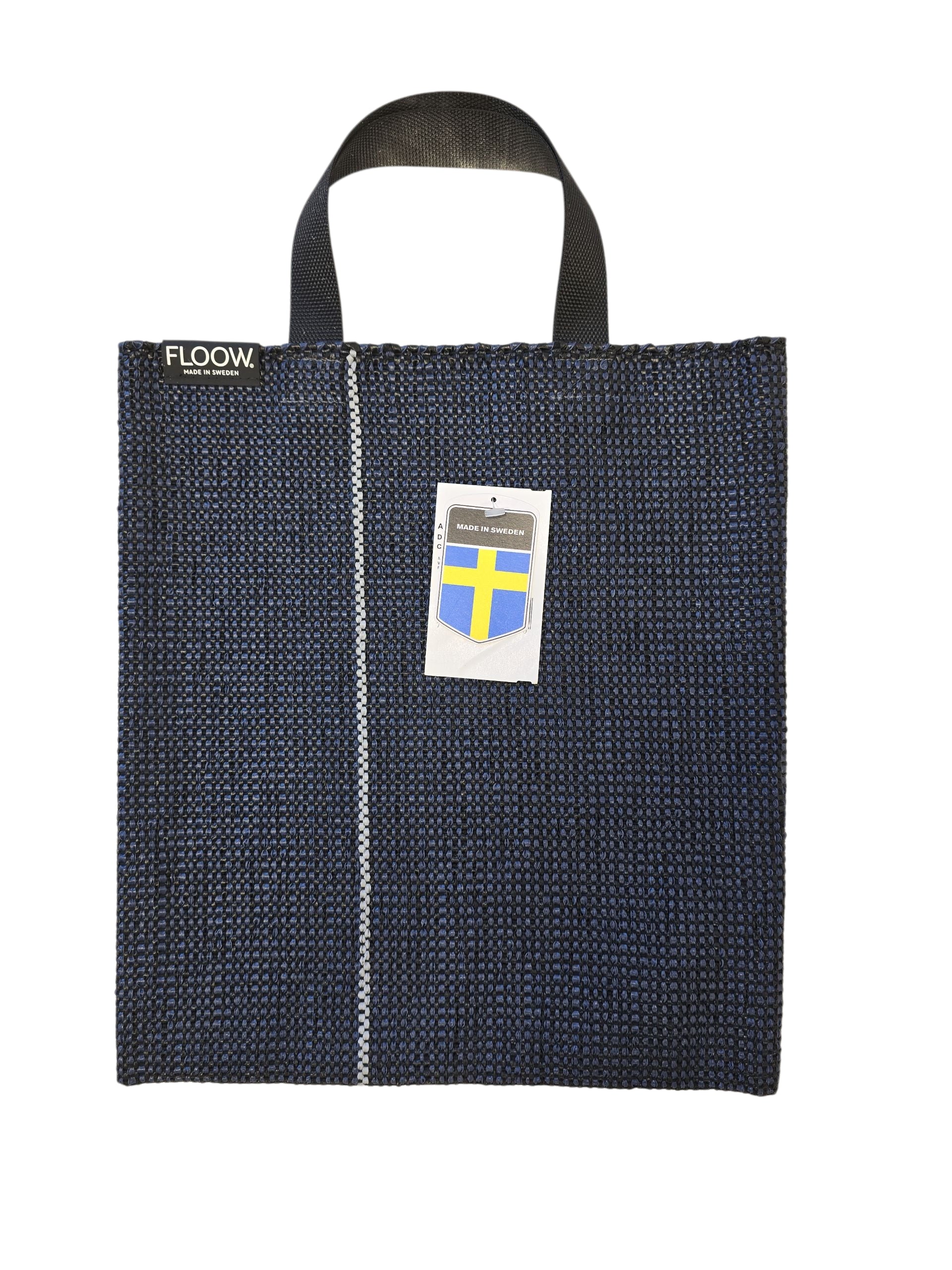 The Horredsmattan Floow Vinyl Bag (32x40cm) is a dark blue tote with black handles, a vertical white stripe, FLOOW. label, Swedish flag tag, and features the iconic Swedish vinyl rug design.