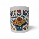 The Swedish Gift Store's "Fika — En Svensk Tradition Kaffepaus" 11oz ceramic mug features colorful folk art with pastries, flowers, leaves, blue birds, and cookies—perfect for a cozy Swedish coffee break.