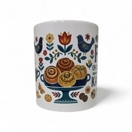 The Swedish Gift Store's "Fika — En Svensk Tradition Kaffepaus" 11oz ceramic mug features colorful folk art with pastries, flowers, leaves, blue birds, and cookies—perfect for a cozy Swedish coffee break.
