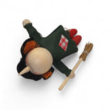 The Kitchen Witch Figurine, handcrafted of wood and felt and measuring 4.5" long, features a green dress, red shoes, orange hair, and a broomstick, lying on its back against a white background.
