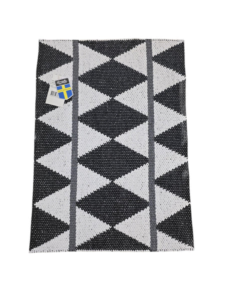 The Horredsmattan Zigge vinyl rug is rectangular and features a black and white geometric pattern with gray stripes on one side and a tag in the top left corner.
