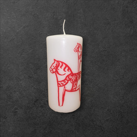 Candle: Red Dala Horse Pillar Candle by Logum Kloster Lys in Denmark—white pillar candle with a red Swedish Dala Horse outline, handcrafted and displayed on a dark textured background.