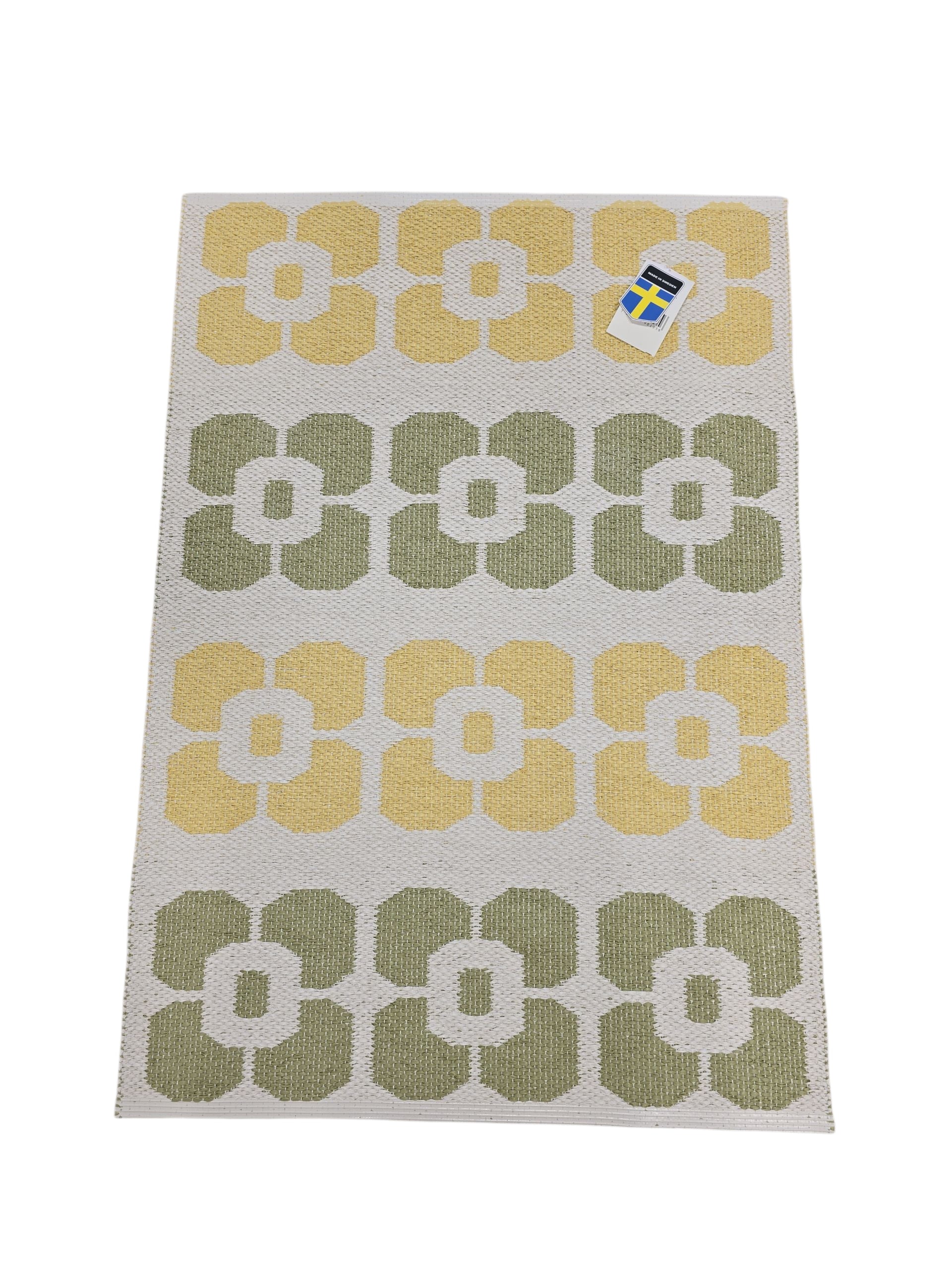 The Horredsmattan Florian vinyl rug features a rectangular shape with a yellow and green geometric flower pattern on a white background, plus a top right tag.