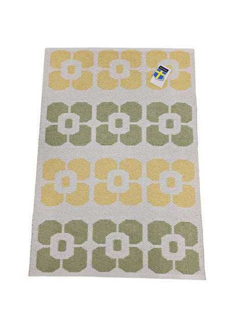 The Horredsmattan Florian vinyl rug features a rectangular shape with a yellow and green geometric flower pattern on a white background, plus a top right tag.