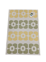 The Vinyl Rug: Horredsmattan - Florian Yellow, Green, & White is a rectangular woven vinyl rug with yellow and green flowers on a white background and a small product tag in one corner.