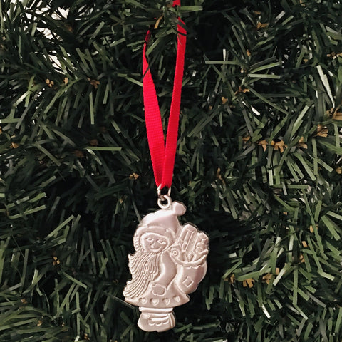 The quaint "Tomte with Gifts" pewter ornament dangles from a green Christmas tree, embellished with a red ribbon.
