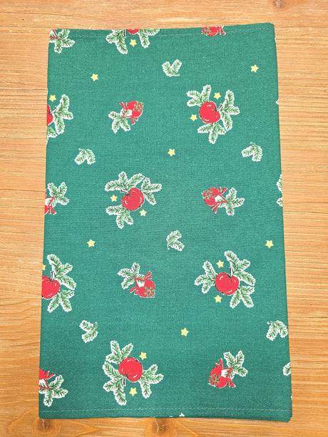 The Runner: Jul Apple Table Runner 36" is made of 100% cotton Swedish fabric with red apples, green leaves, and small yellow stars, shown flat on a wooden surface.