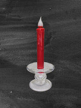 A red wax candle with drips stands in a clear Glass Dual-Size Reversible Candle Holder for taper, ball, or pillar candles, set against a dark textured background.