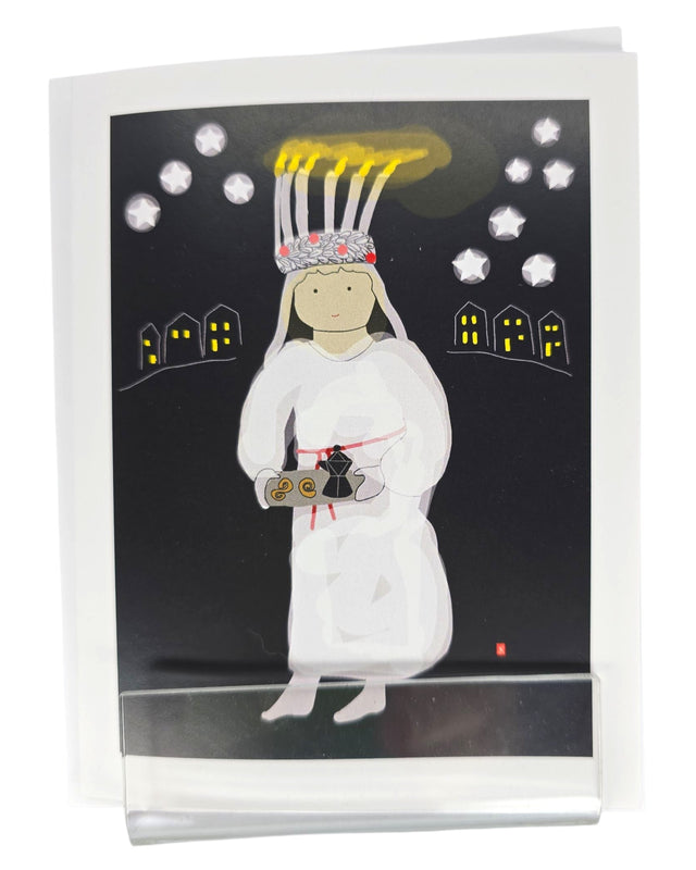 The Card: Lucia Greeting Card by Lisa Rydin Erickson features a girl in a white dress with a candle crown, holding pastries on a Fika tray, set among glowing houses—a charming Scandinavian holiday card. Blank inside with envelope included.