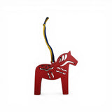 A red laser-cut Dala Horse ornament with Kurbits design, featuring a blue and yellow ribbon, handcrafted in Sweden, shown on a plain white background.