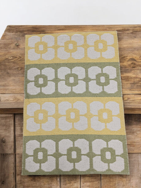 The Horredsmattan Florian Vinyl Rug features rows of stylized white flowers in yellow, green, and gray. Durable and eco-friendly, this modern rectangular rug looks stunning on wooden surfaces.