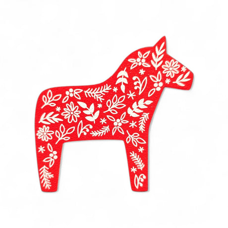 A handcrafted Magnet: Red Swedish Dala Horse with White Kurbits Refrigerator Magnet, featuring white floral and leaf patterns, is set against a plain white background.