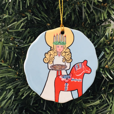 The "Ornament: Saint Lucia with Dala Horse Ceramic" adds a unique charm to a Christmas tree with its depiction of Saint Lucia holding a tray beside a red Dala horse.