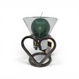A green candle in a Leif Cup for Ball Candle sits on the Talla Imports Danish Iron Candle Holder with Heart, with a product tag behind it and a white background.