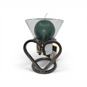 A green candle in a Leif Cup for Ball Candle sits on the Talla Imports Danish Iron Candle Holder with Heart, with a product tag behind it and a white background.