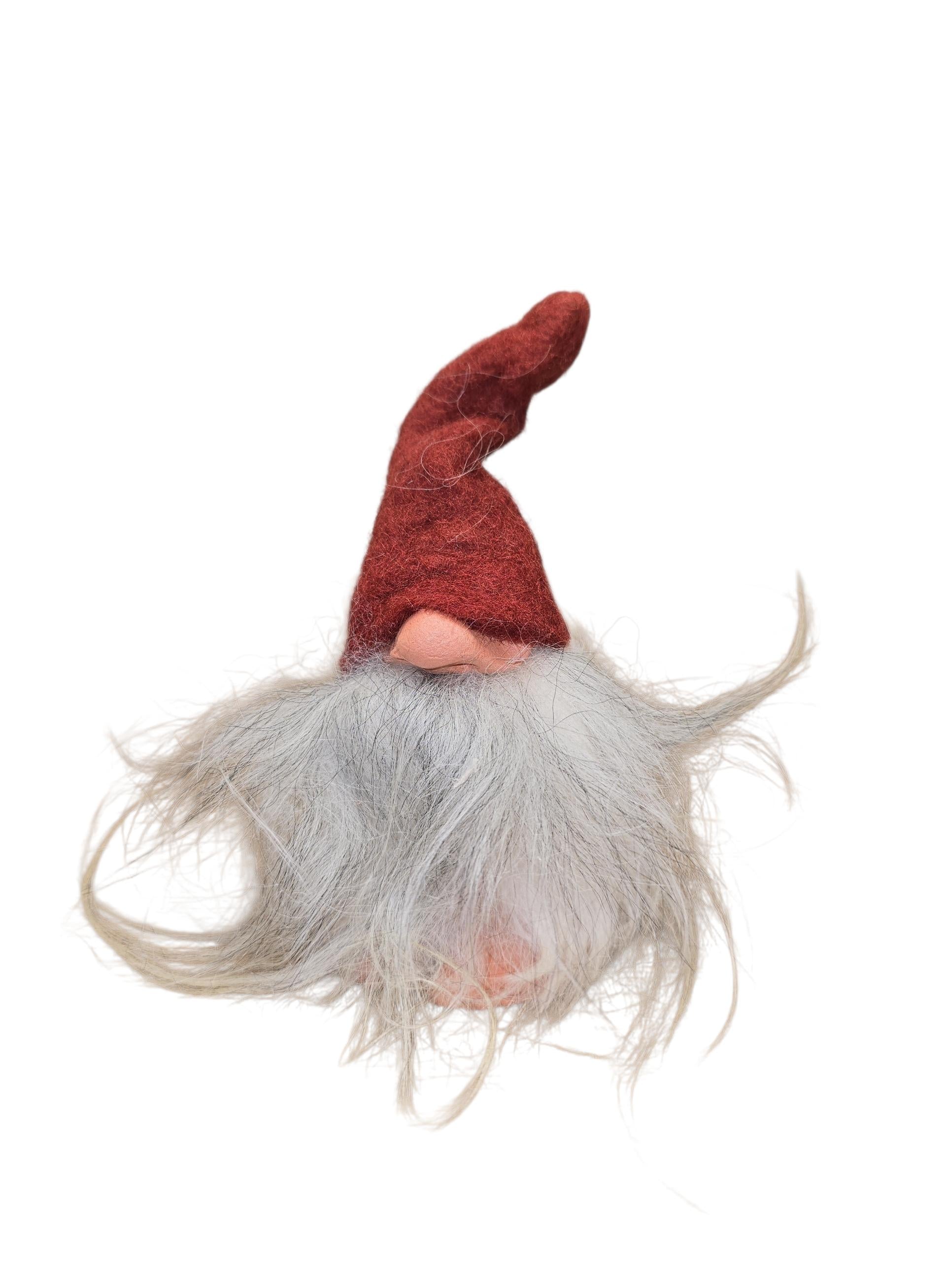 A handcrafted Swedish "Foot Tomte" gnome figurine by Gumselids, 6" tall with a clay nose and feet, sheep's wool gray beard, and tall red pointed hat, isolated on white background.