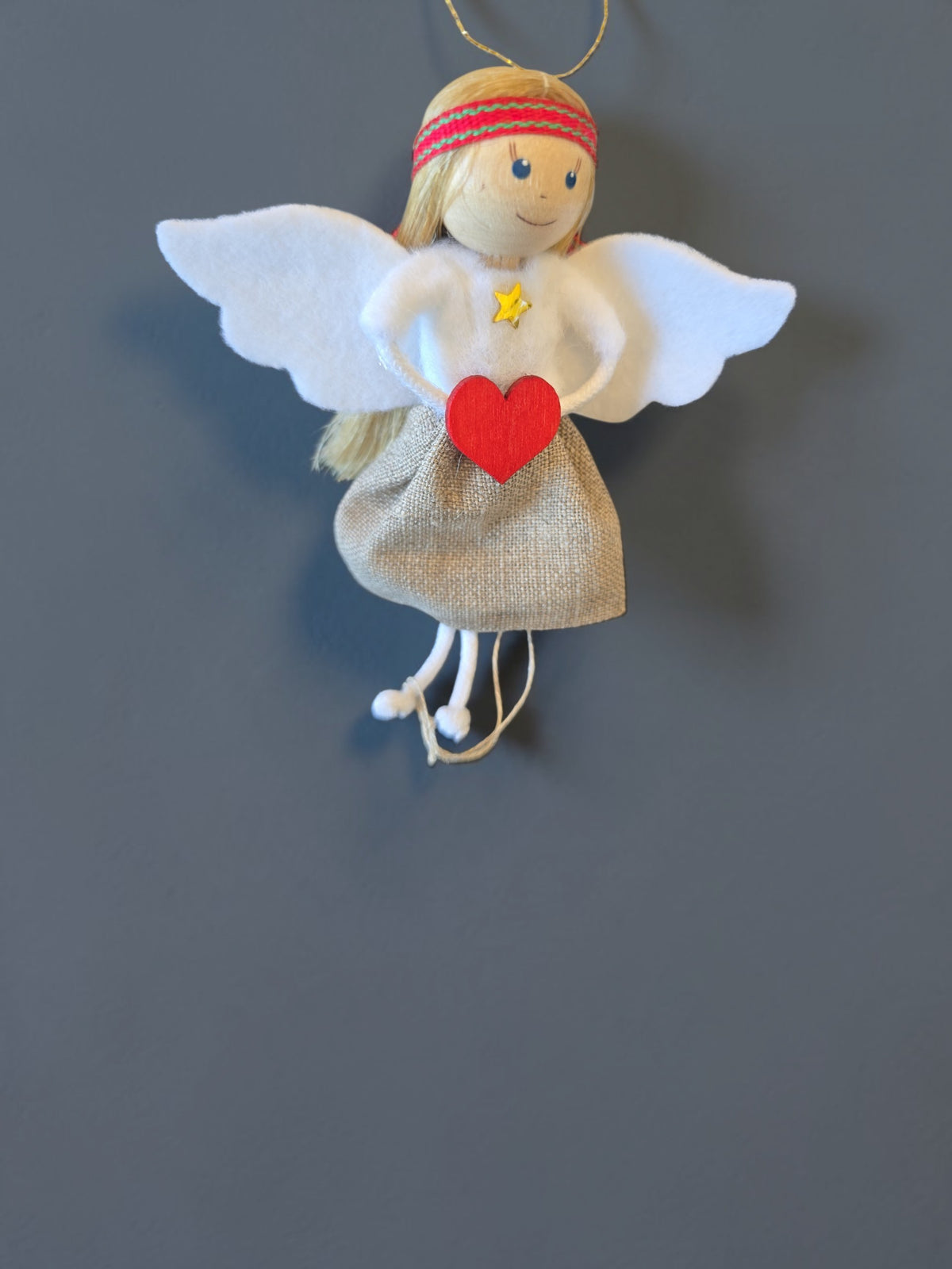 Scandinavian angel ornament with blonde hair, white felt wings, a beige linen skirt, and a red wooden heart.