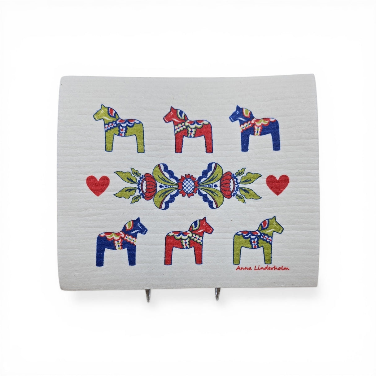 The Dish Cloth: Six Dala Horses with Swedish Kurbits "Flowers" shows six colorful Dala horses, three red hearts, a central floral pattern, and the artist Anna Linderholm's name in the lower right corner.