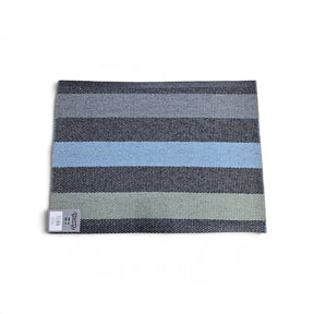 Rectangular woven vinyl rug with horizontal gray, black, and light blue stripes and a small Swedish flag tag.