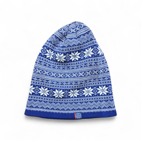 The Hat: Northern Story Setesdal Hat is made from 100% Merino wool in royal blue, featuring white geometric and snowflake designs in a classic Norwegian star pattern. Displayed flat on a white background.