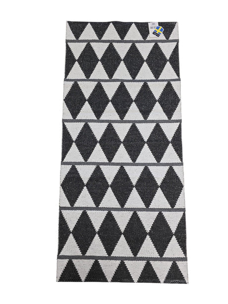 The Vinyl Rug: Horredsmattan - Zigge features a rectangular woven design with a black and white geometric diamond pattern, gray stripes on one side, and a small corner tag.