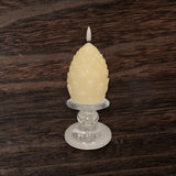 A cream-colored, artichoke-shaped candle rests on a Glass Dual-Size Reversible Candle Holder for taper, ball, or pillar candles, set against a dark wooden background.