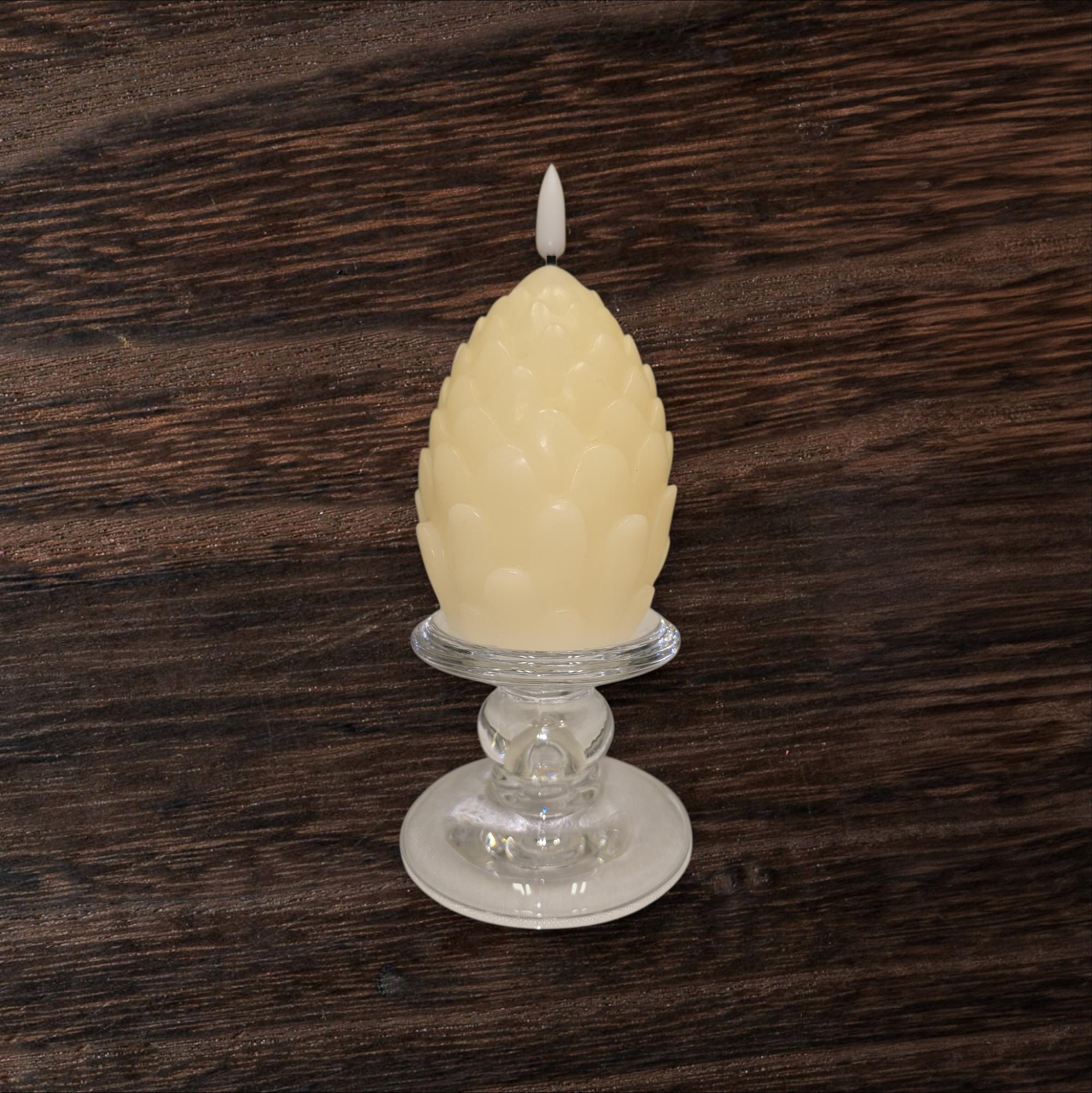 A cream-colored, artichoke-shaped candle rests on a Glass Dual-Size Reversible Candle Holder for taper, ball, or pillar candles, set against a dark wooden background.
